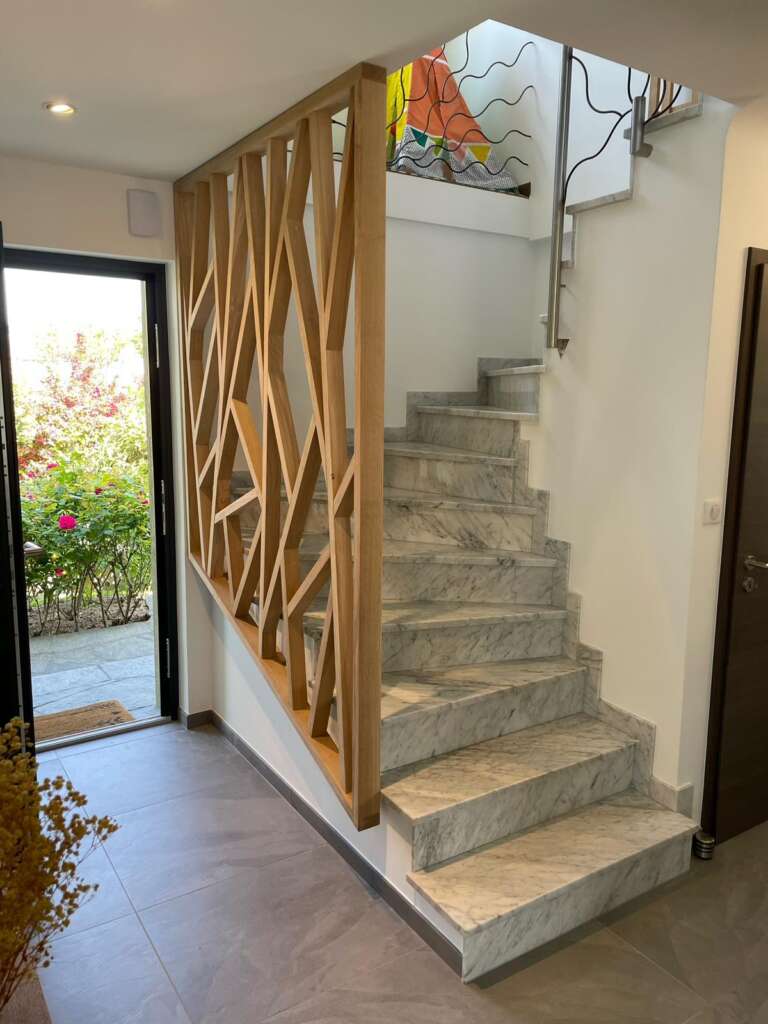Garde-corps en bois à motif géométrique au pied d’un escalier, vu depuis l’entrée